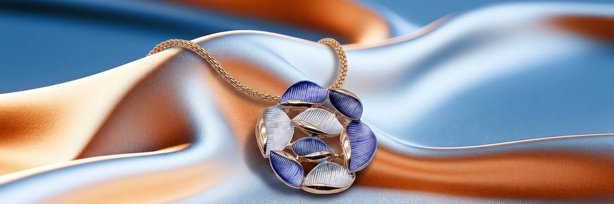 Goldfarbene Halskette mit blau-weissem Blätter-Anhänger auf blau-orangem Stoff.