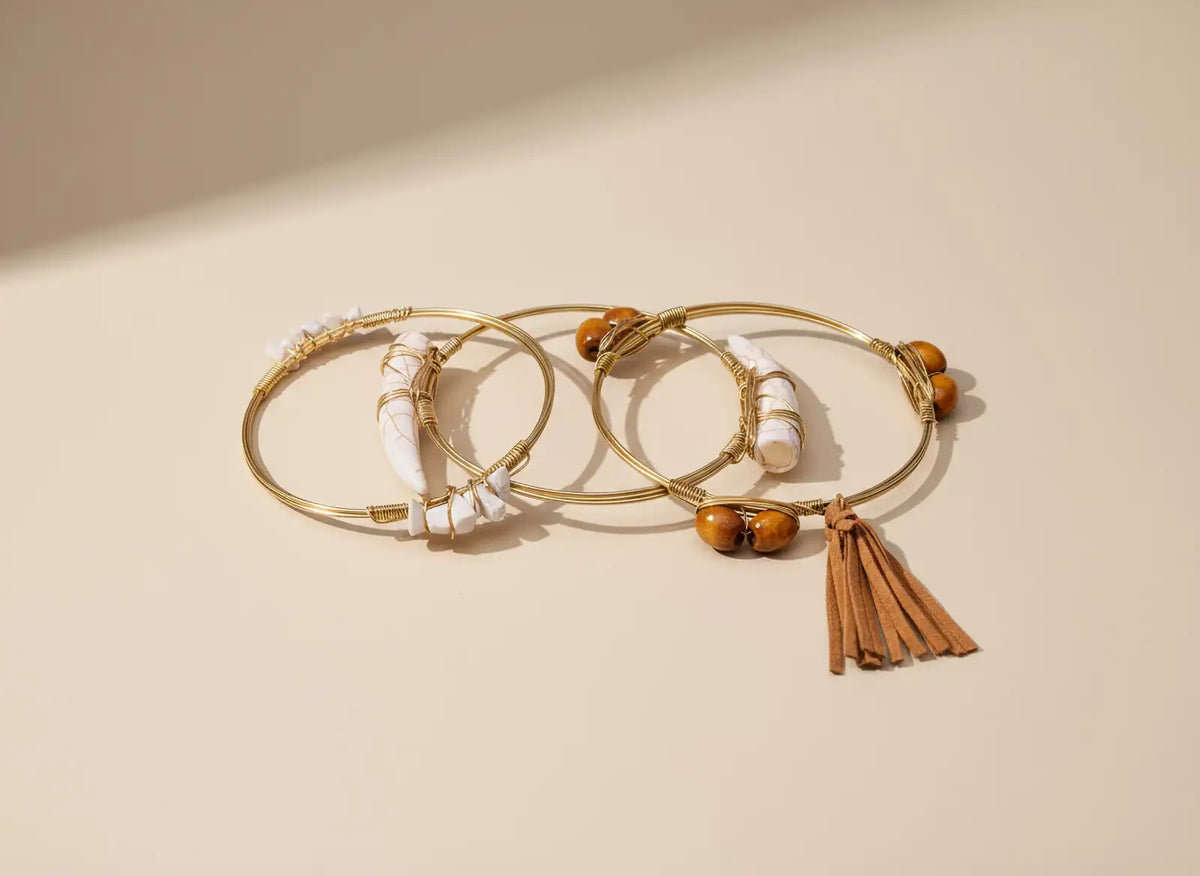 Emotionaler Schmuck in sanftem Licht – goldfarbene Armreifen mit Naturmaterialien. Avirelle.