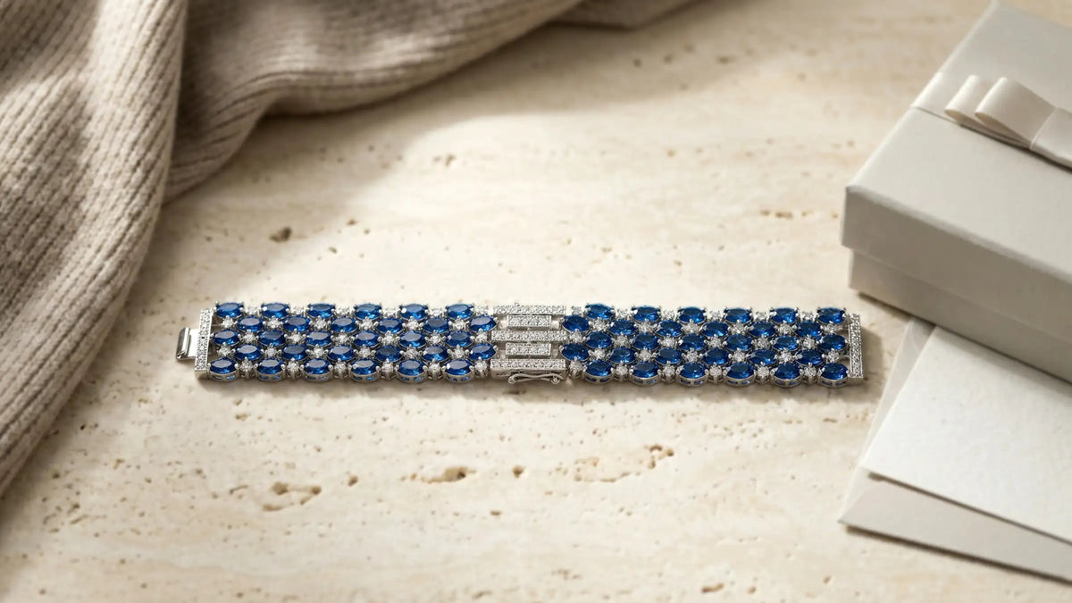 Silberfarbenes Armband mit blauen Zirkonia-Steinen auf hellem Stein neben Geschenkbox, Avirelle.