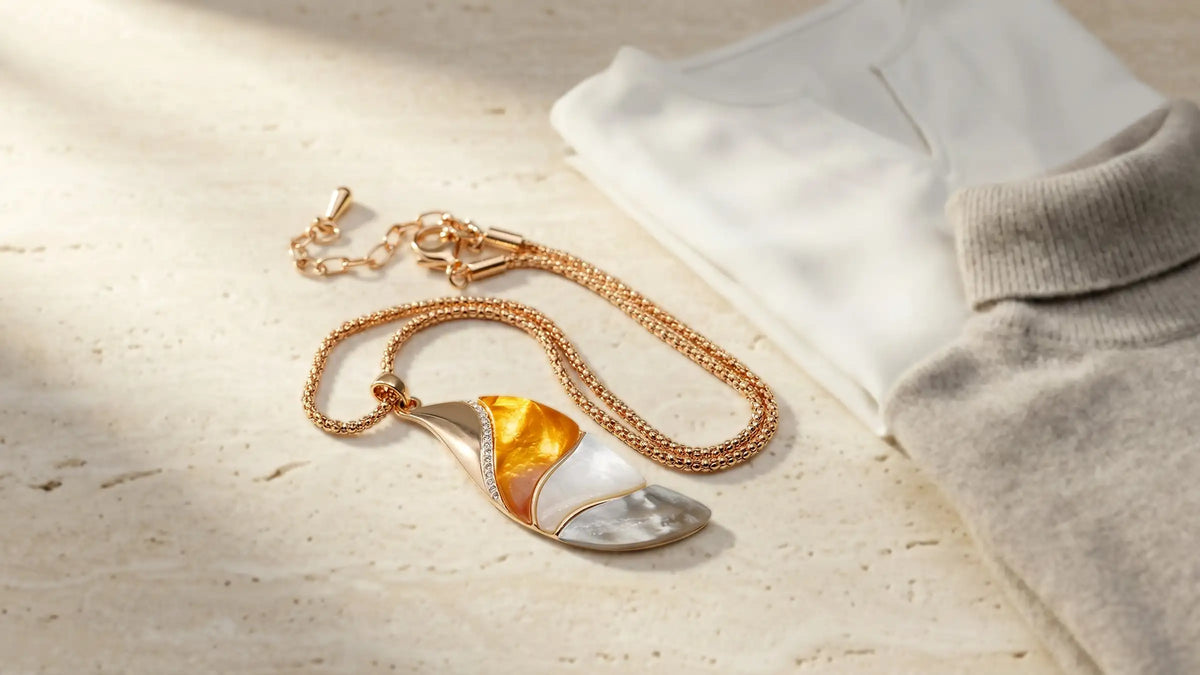 Roségoldfarbenes Collier mit Perlmutt-Anhänger auf Stein neben Bluse und Rollkragen, Avirelle.