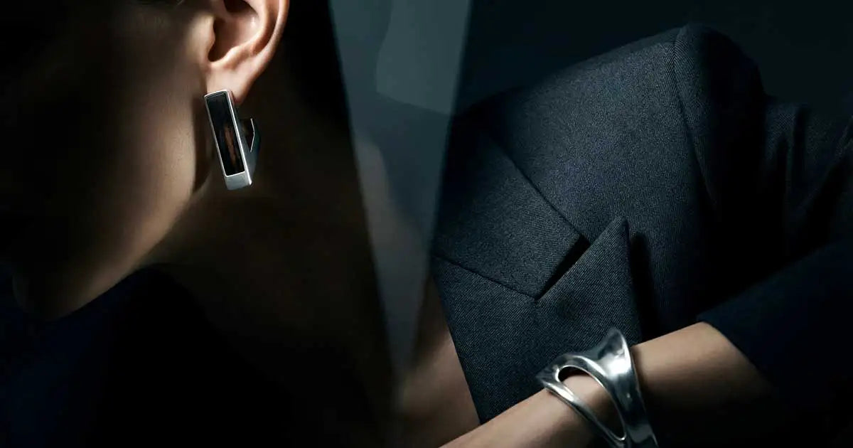 Minimalistischer silberfarbener Business-Schmuck für Frauen vor einem modernen Architektur-Hintergrund.