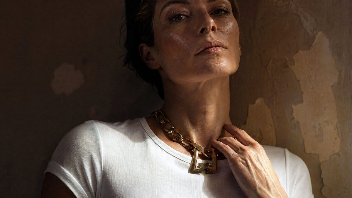 Ein schlichtes weisses T-Shirt für Damen aus Baumwolle kombiniert mit einer massiven, goldfarbenen Gliederkette auf einem hellen Hintergrund.